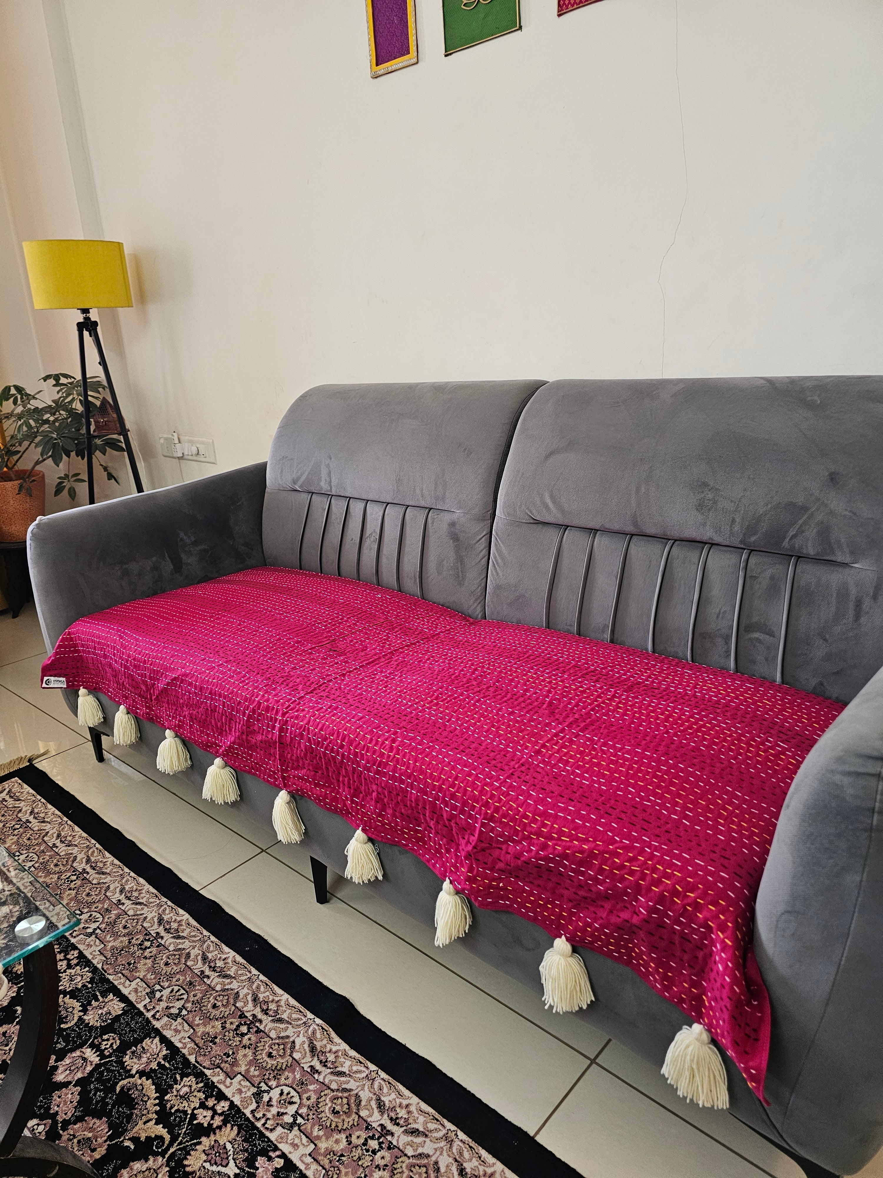 Gray sofa with a pink blanket featuring white tassels in a living room setting.