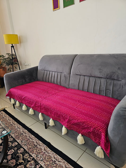 Gray sofa with a pink blanket featuring white tassels in a living room setting.