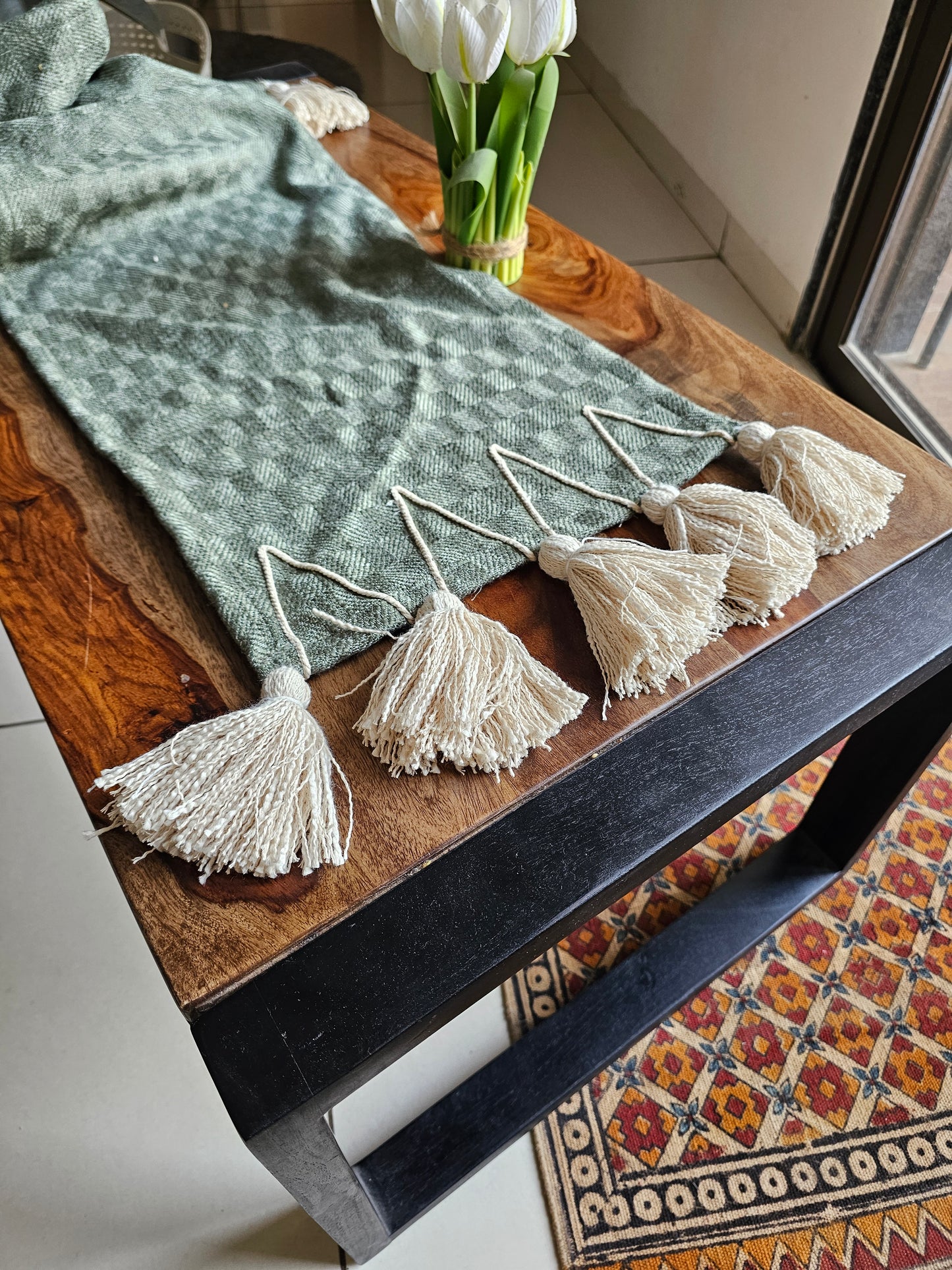 Green textured blanket with tassels on a wooden surface, next to white tulips.