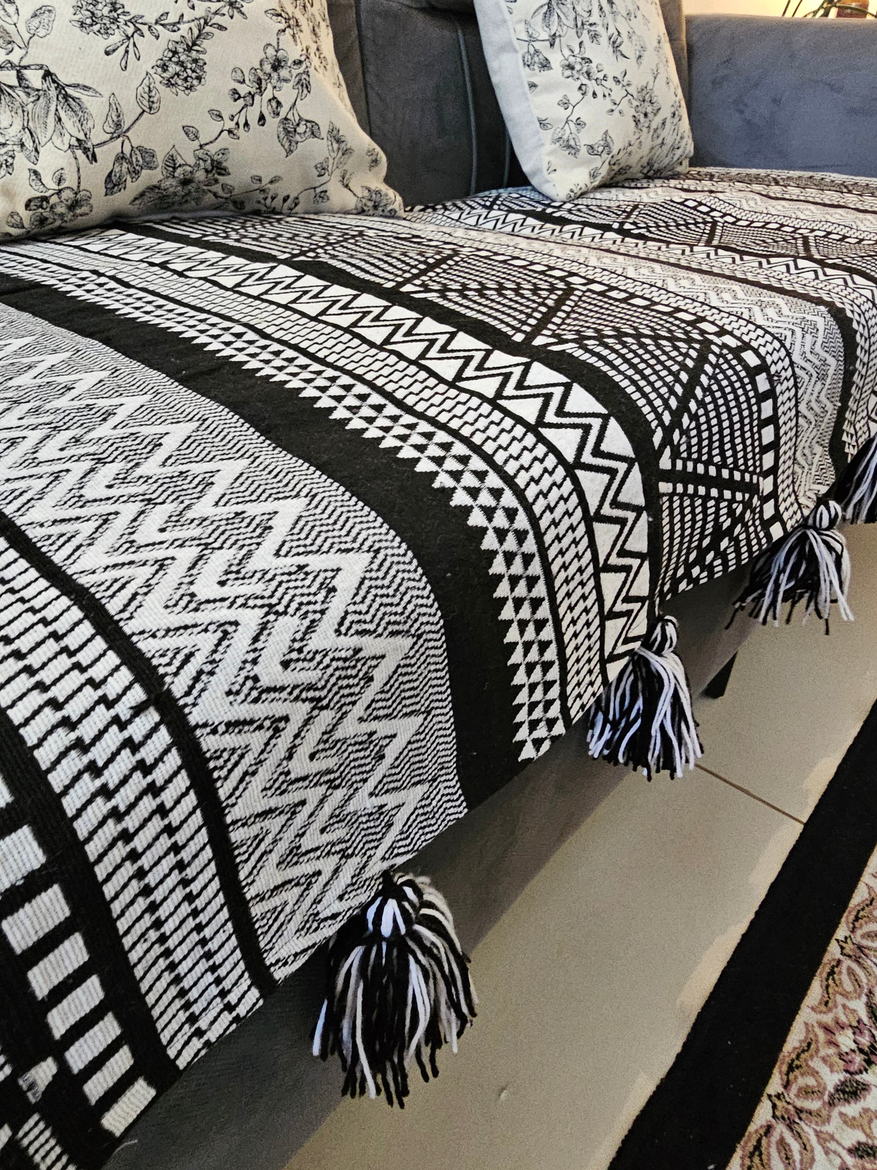 Black and white patterned throw blanket with tassels on a sofa.