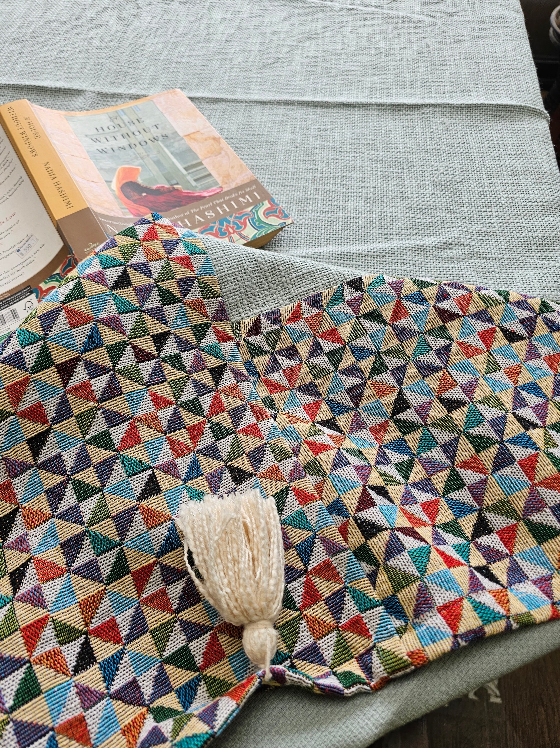 Multicolored geometric-patterned blanket with a tassel on a gray surface