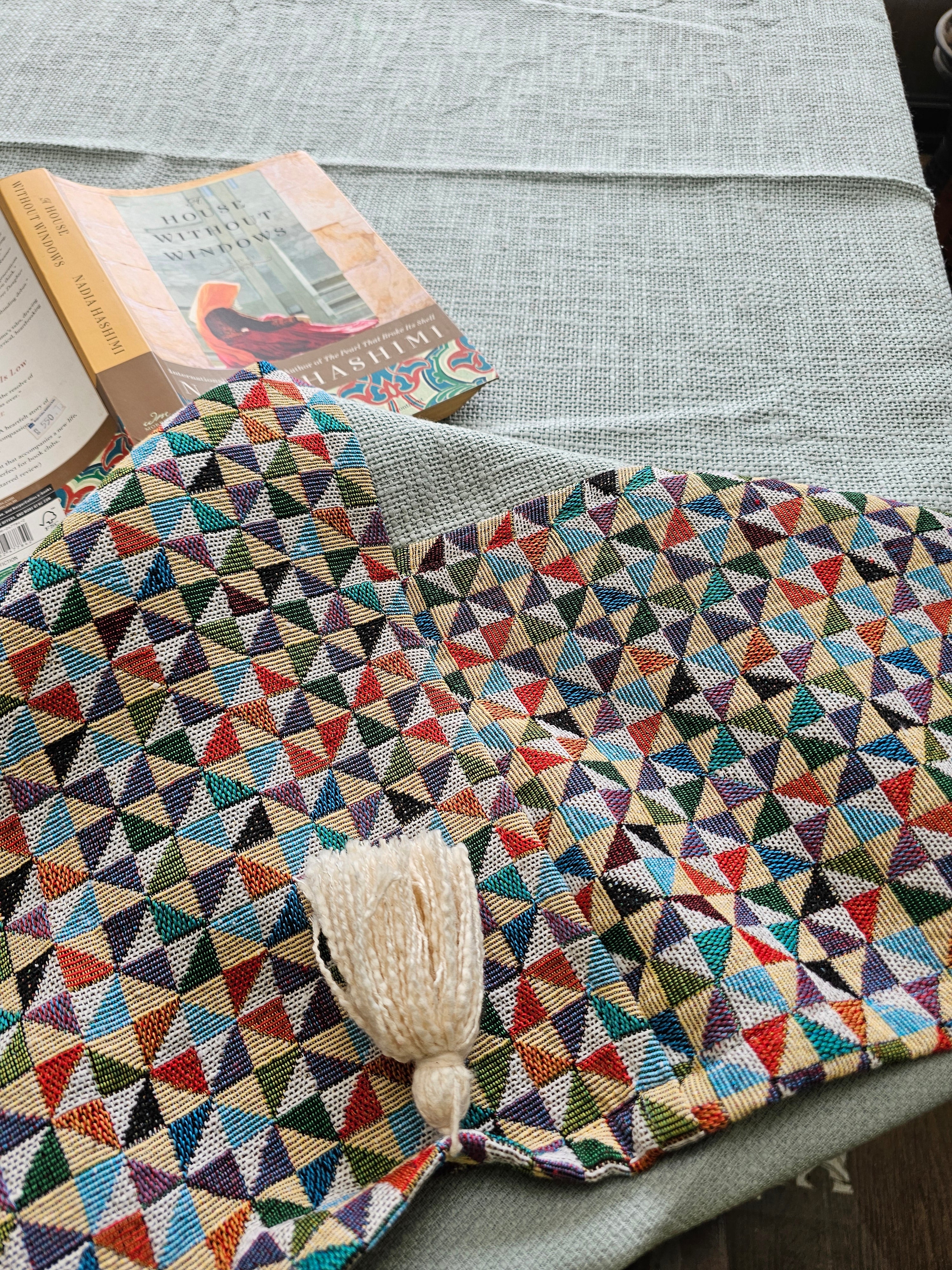 Multicolored geometric-patterned blanket with a tassel on a gray surface