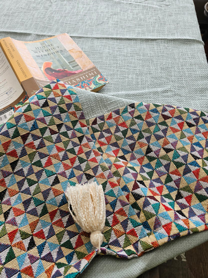 Multicolored geometric-patterned blanket with a tassel on a gray surface
