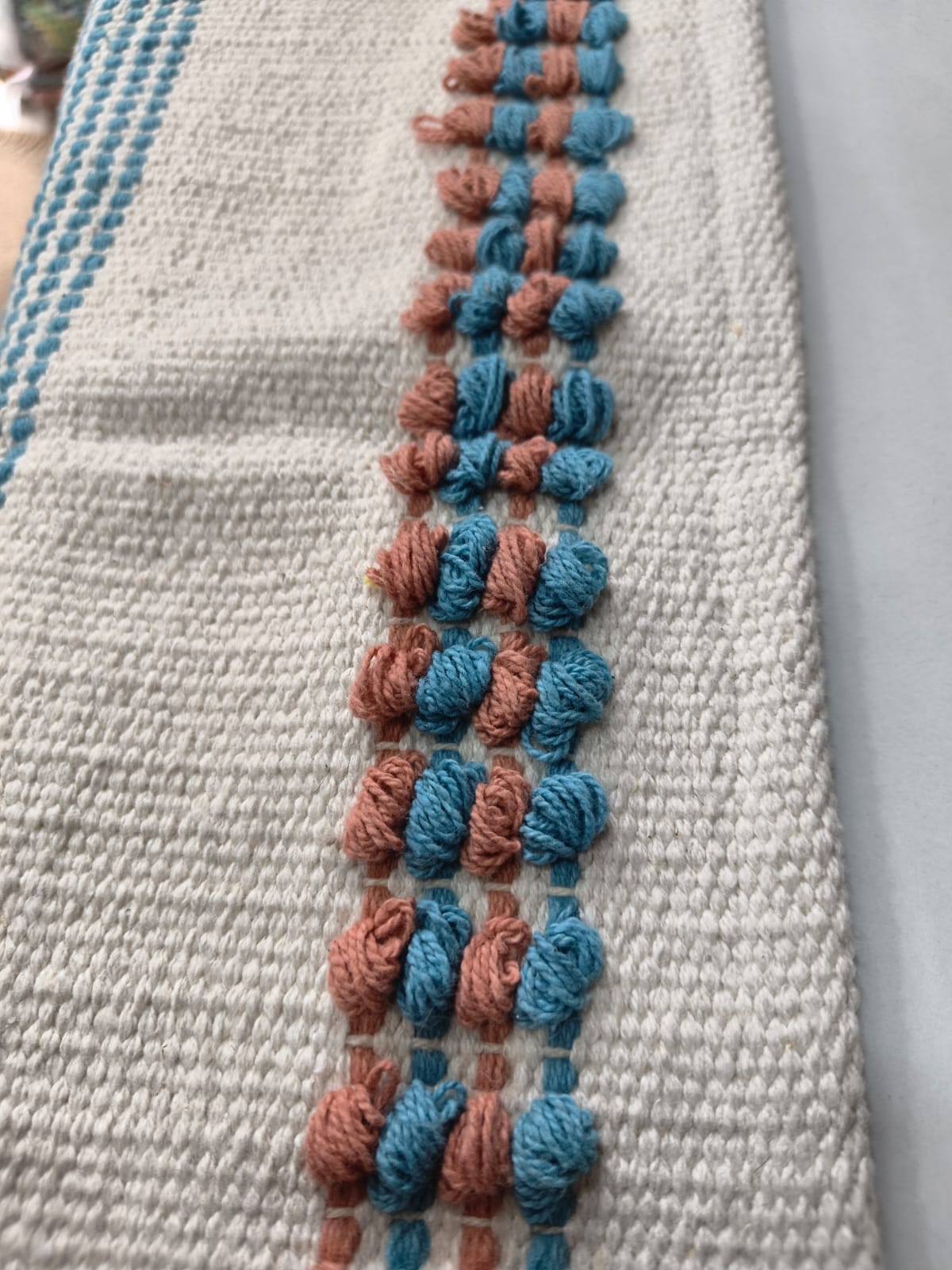 Close-up of an ivory handwoven cotton tufted rug featuring chunky alternating blue and peach tufted knots and delicate blue side stripes.