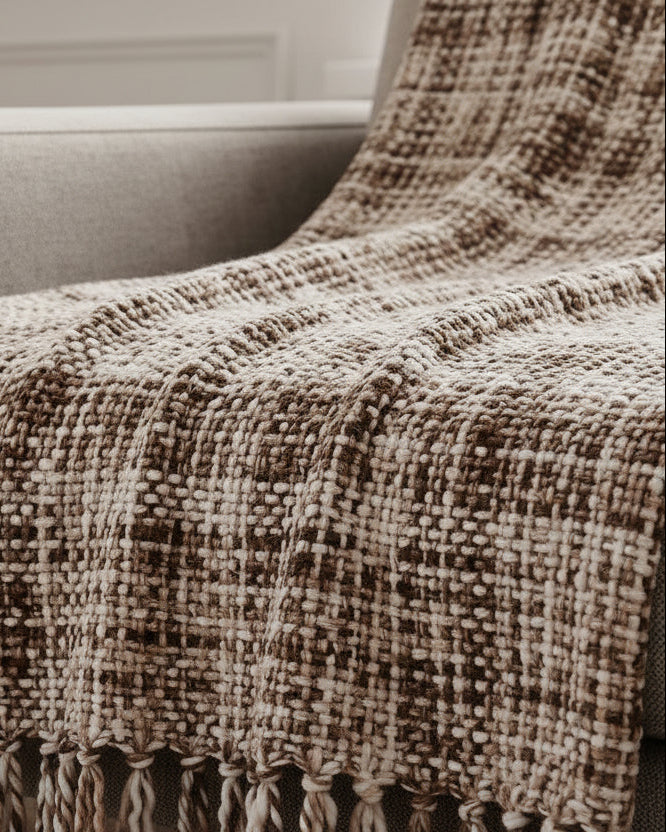 Ivory and walnut brown handwoven woolen sofa throw blanket with windowpane plaid pattern and twisted fringe draped over a grey sofa.