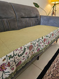 Decorative table runner with floral pattern on a table next to a gray sofa.