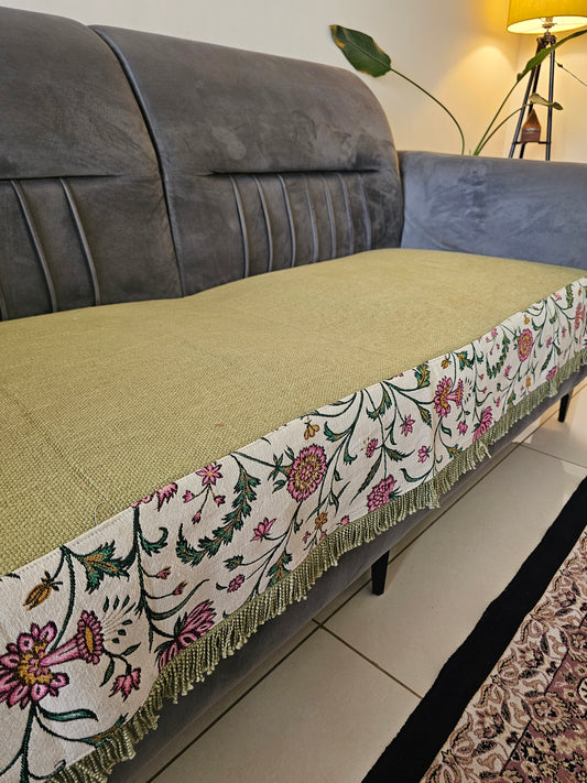 Decorative table runner with floral pattern on a table next to a gray sofa.