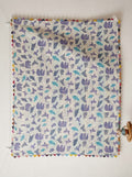 Hanging off-white cotton baby quilt featuring purple and teal origami animal motifs with hand-stitched Kantha quilting and colorful triangle edge binding.