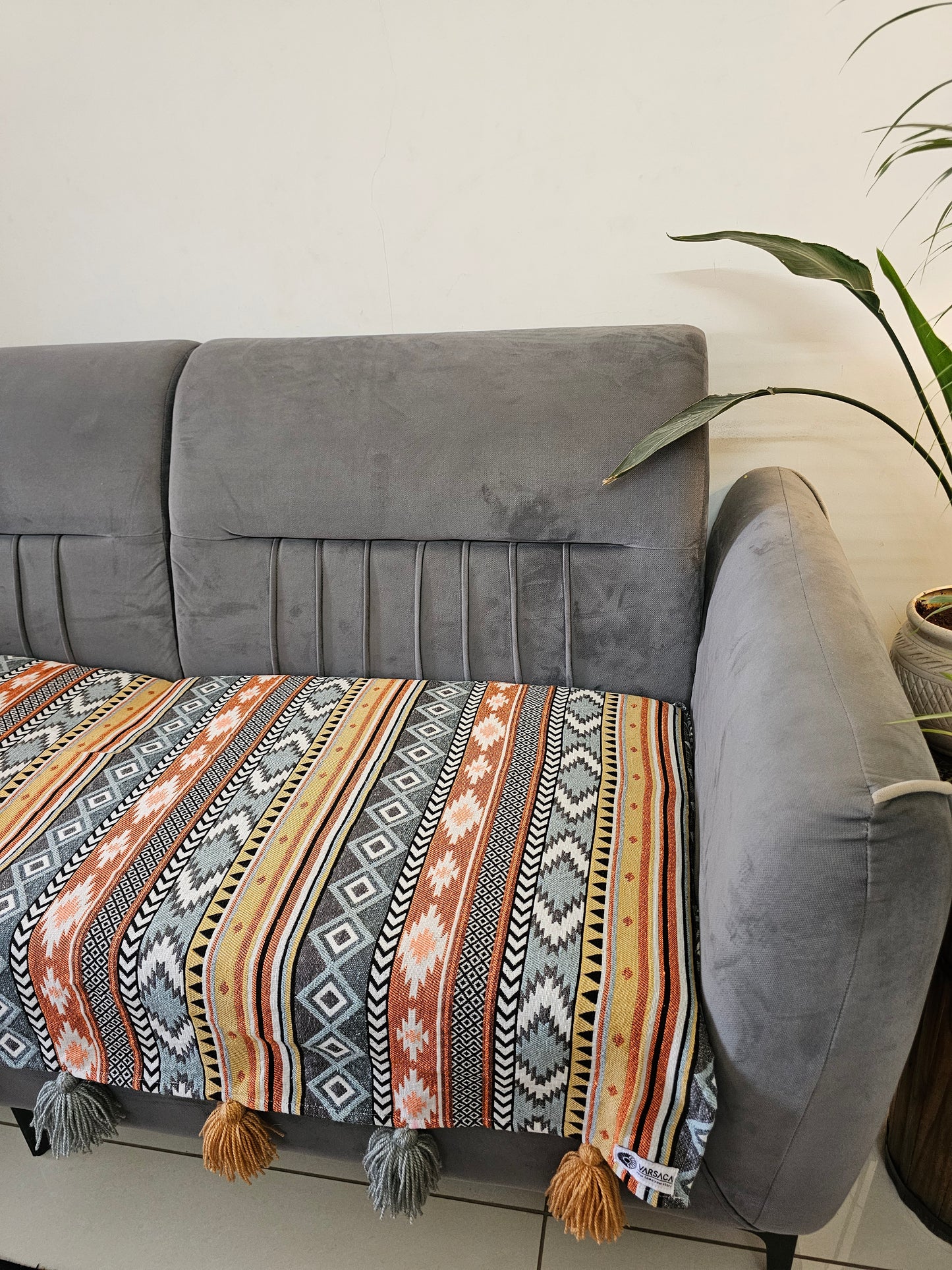 Gray armchair with a patterned throw blanket draped over it, against a neutral background.