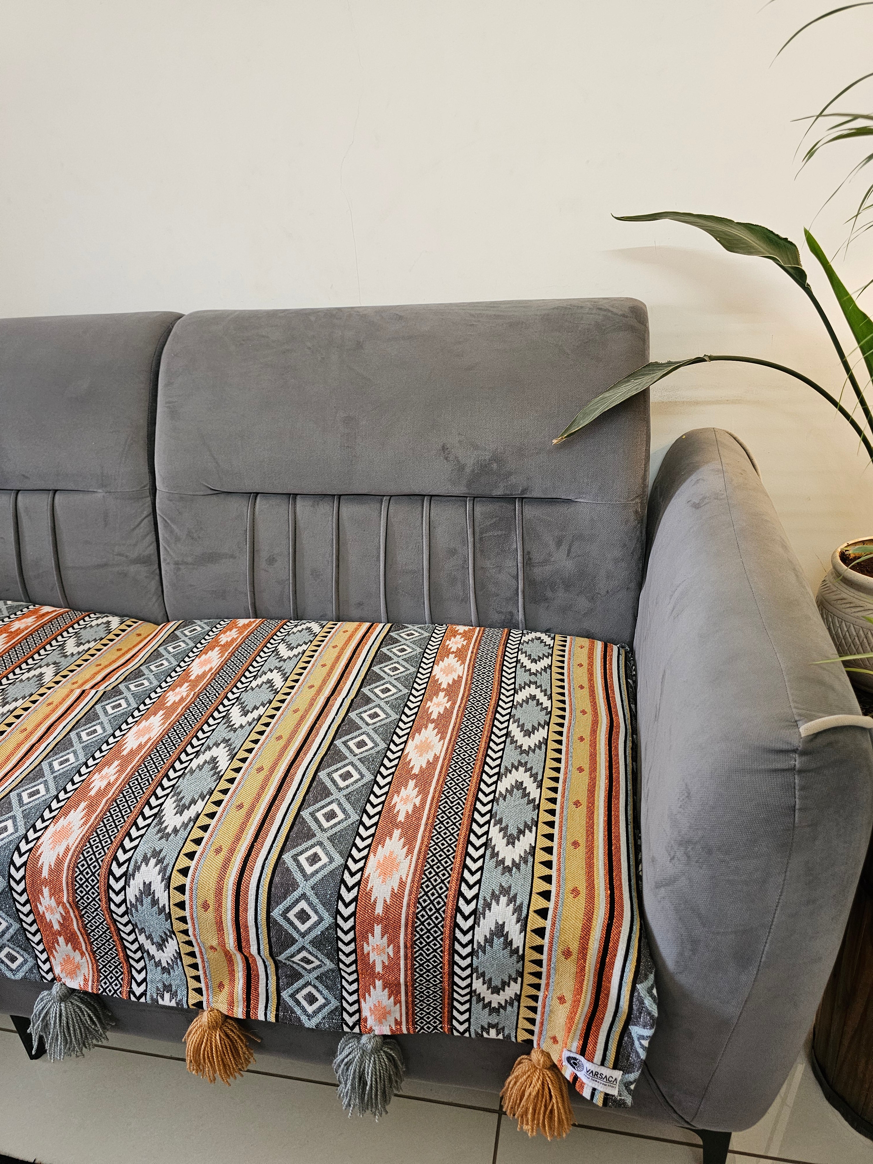 Gray armchair with a patterned throw blanket draped over it, against a neutral background.