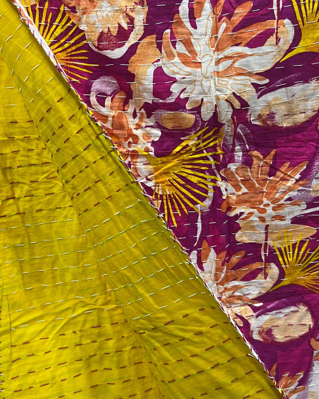 Magenta and mustard floral cotton kantha table cover featuring traditional running hand-stitching and a reversible solid yellow backing in a dining setup.