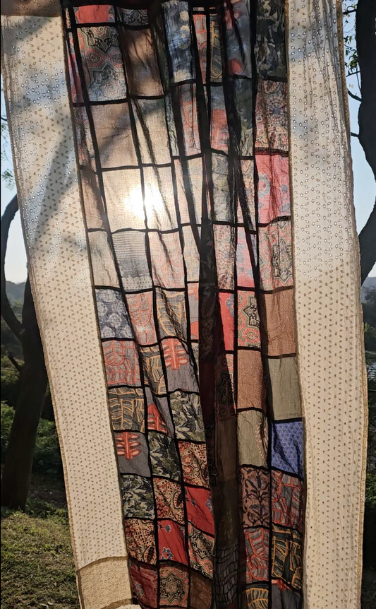 Textile with a pattern of squares in various colors, held up outdoors.