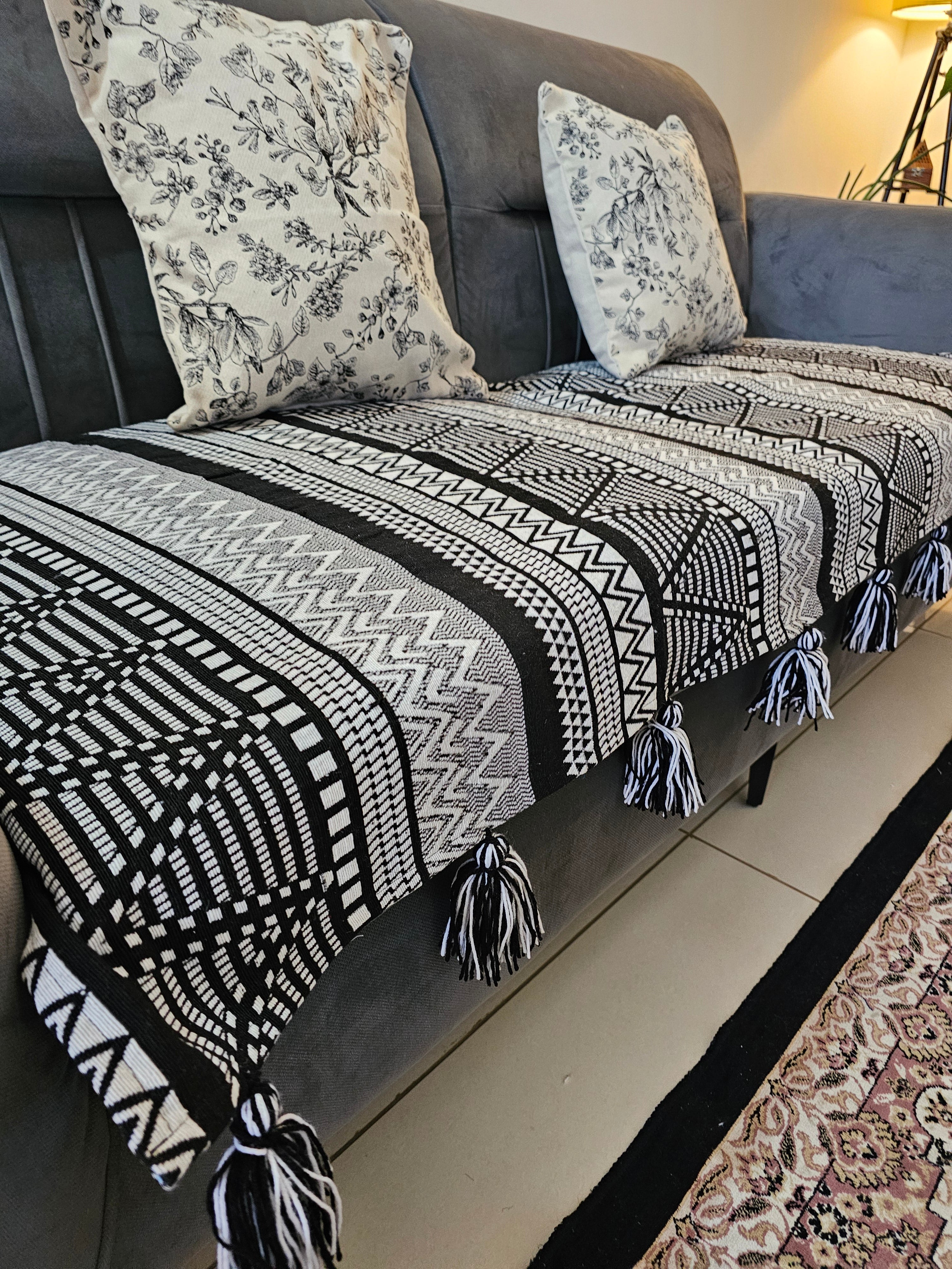 Black and white patterned throw blanket with tassels draped over a sofa with floral cushions.