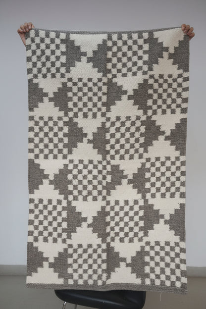 Person holding a patterned blanket with geometric design in a room setting.