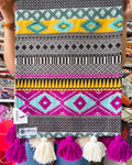 Multicolor Aztec Jacquard cotton dining table runner featuring vibrant geometric tribal bands and alternating magenta and off-white woolen hanging tassels, with Vasaca brand labels.