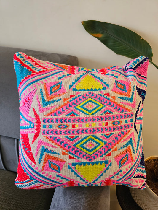 Colorful geometric patterned pillow on a gray surface with a plant leaf in the background