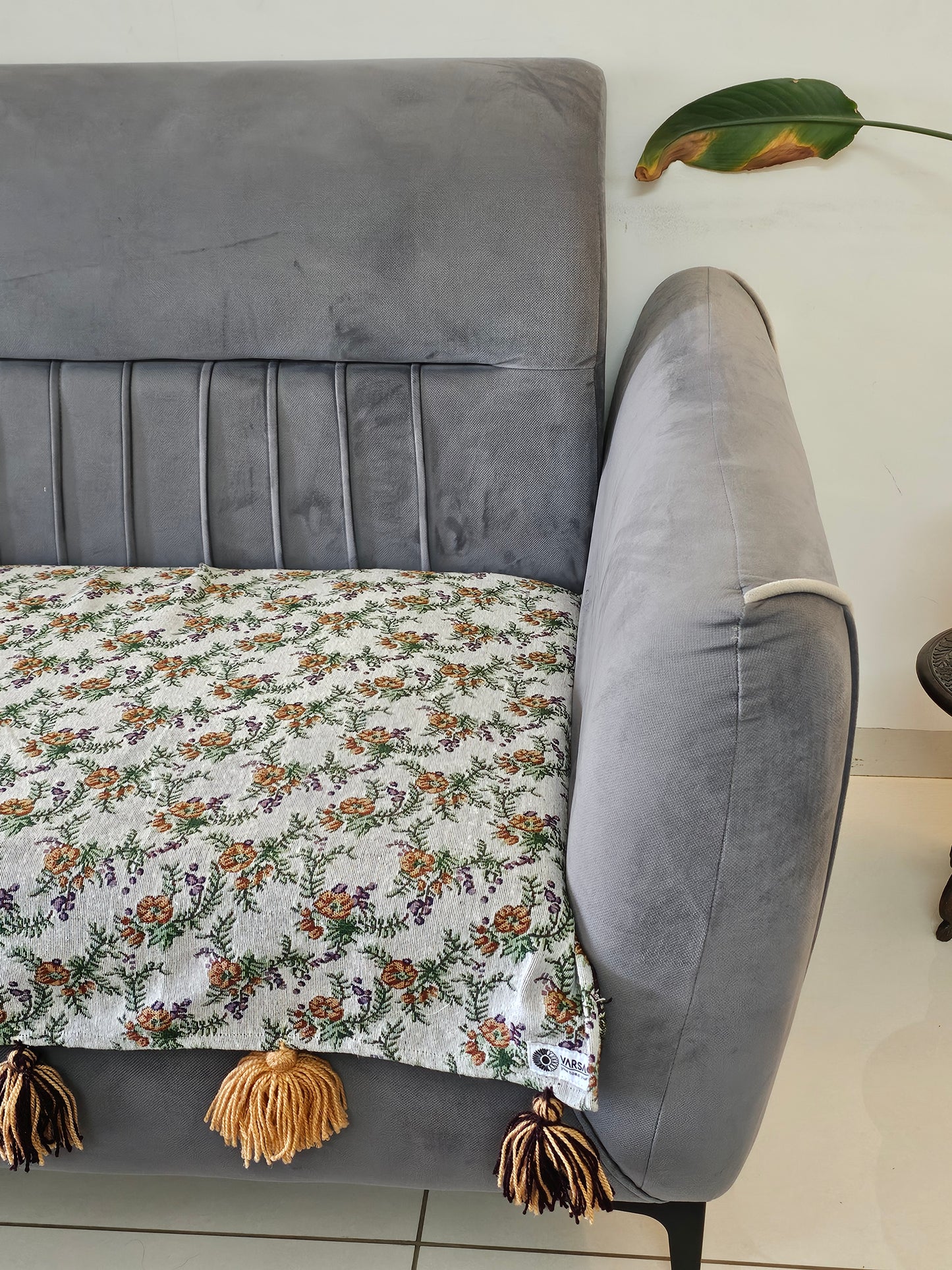 Gray sofa with a floral blanket draped over it, on a tiled floor.