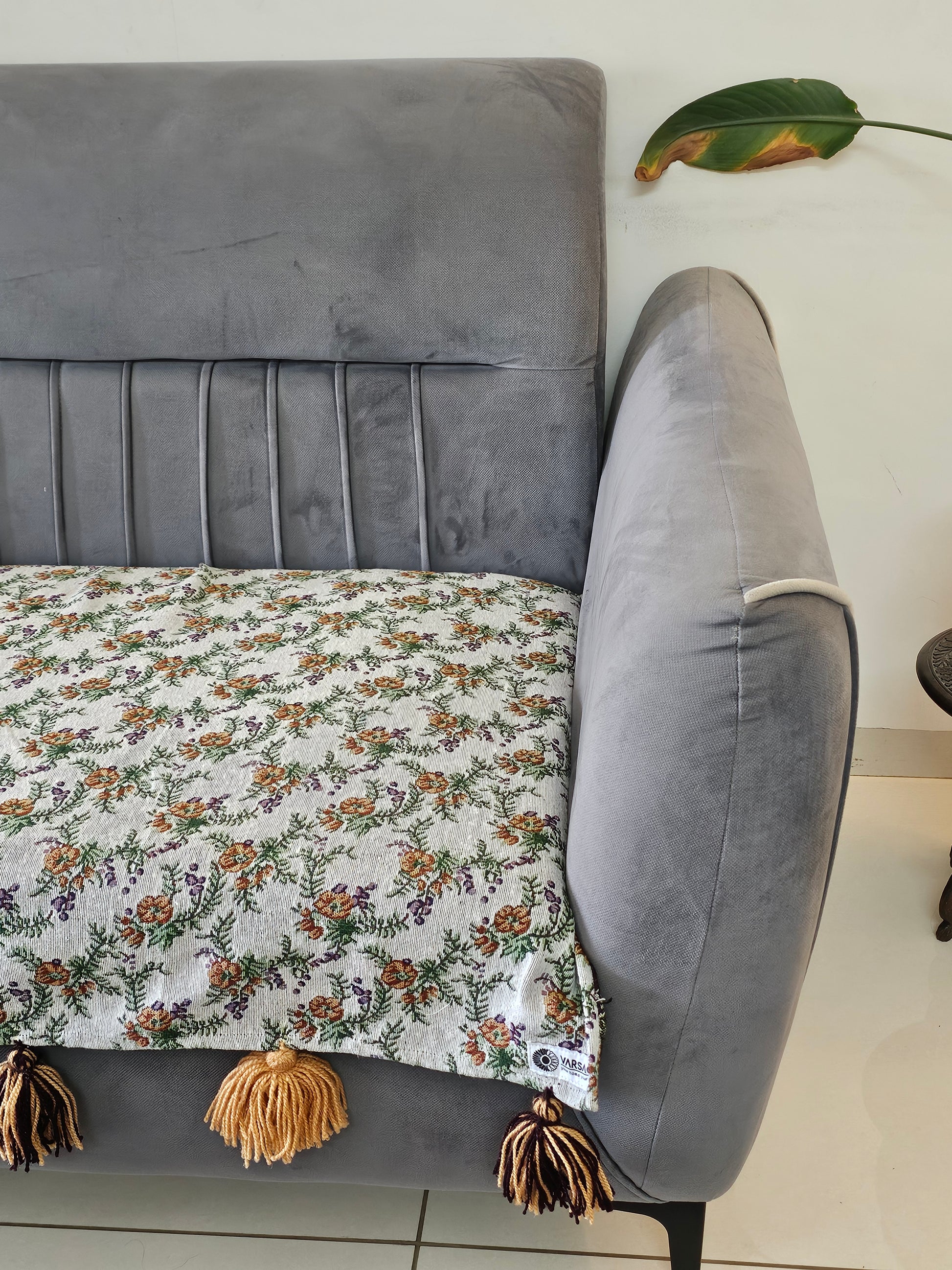 Gray sofa with a floral blanket draped over it, on a tiled floor.
