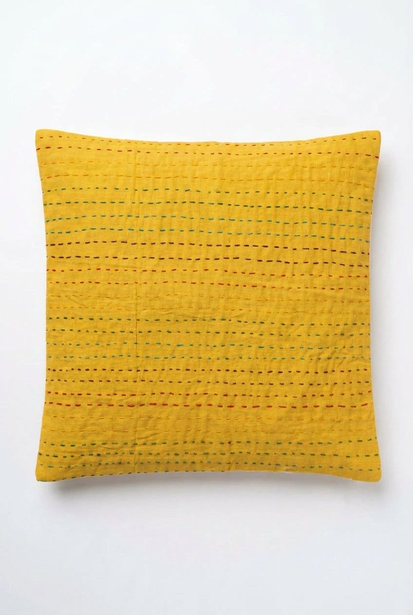 Square mustard yellow cotton cushion cover with horizontal multicolored Kantha hand stitching laid flat on a light floor surface.
