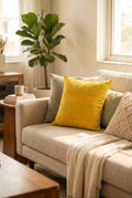 Square mustard yellow cotton cushion cover with horizontal multicolored Kantha hand stitching laid flat on a light floor surface.
