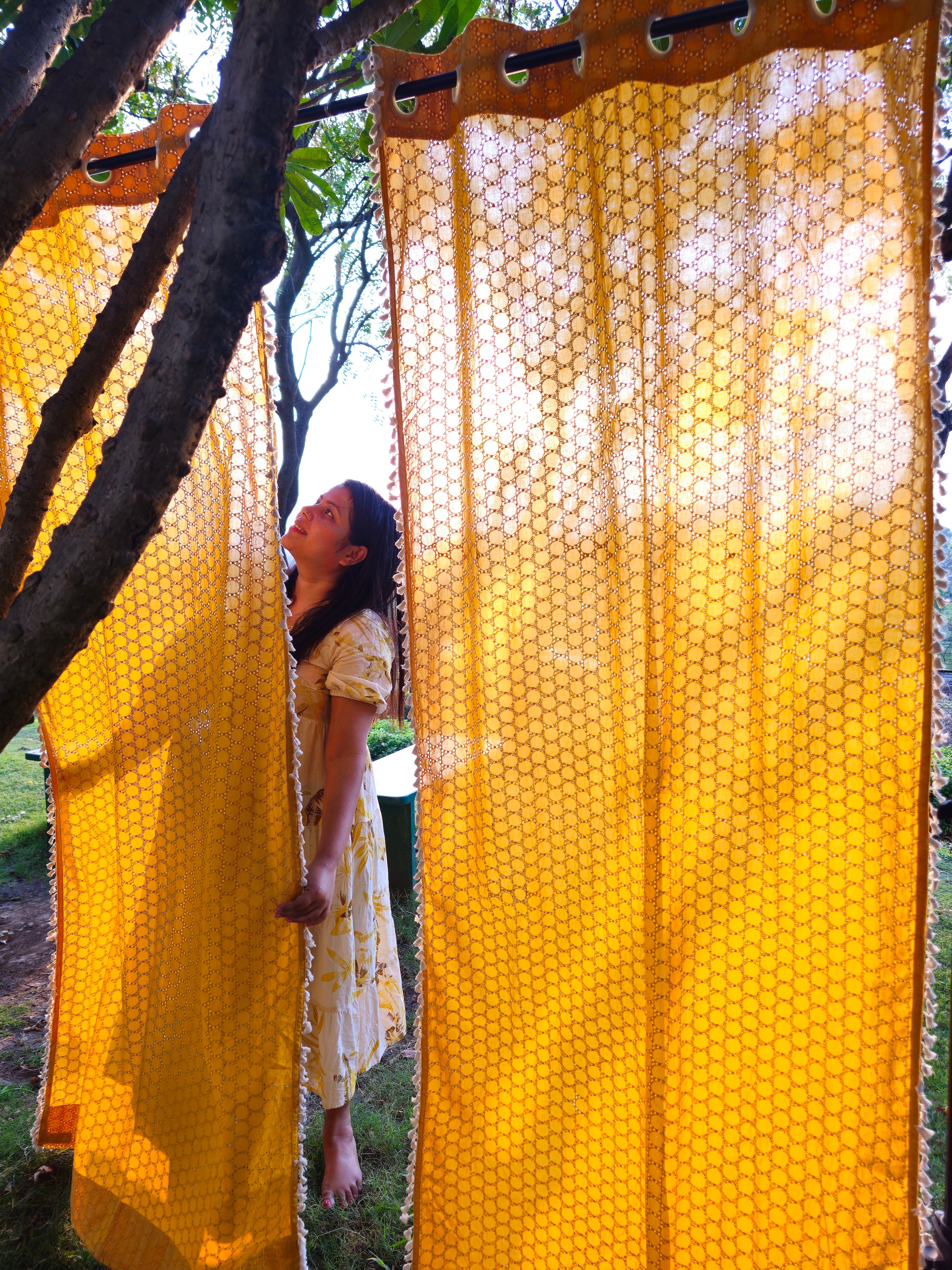 Woman standing behind a yellow honeycomb-patterned curtain outdoors.