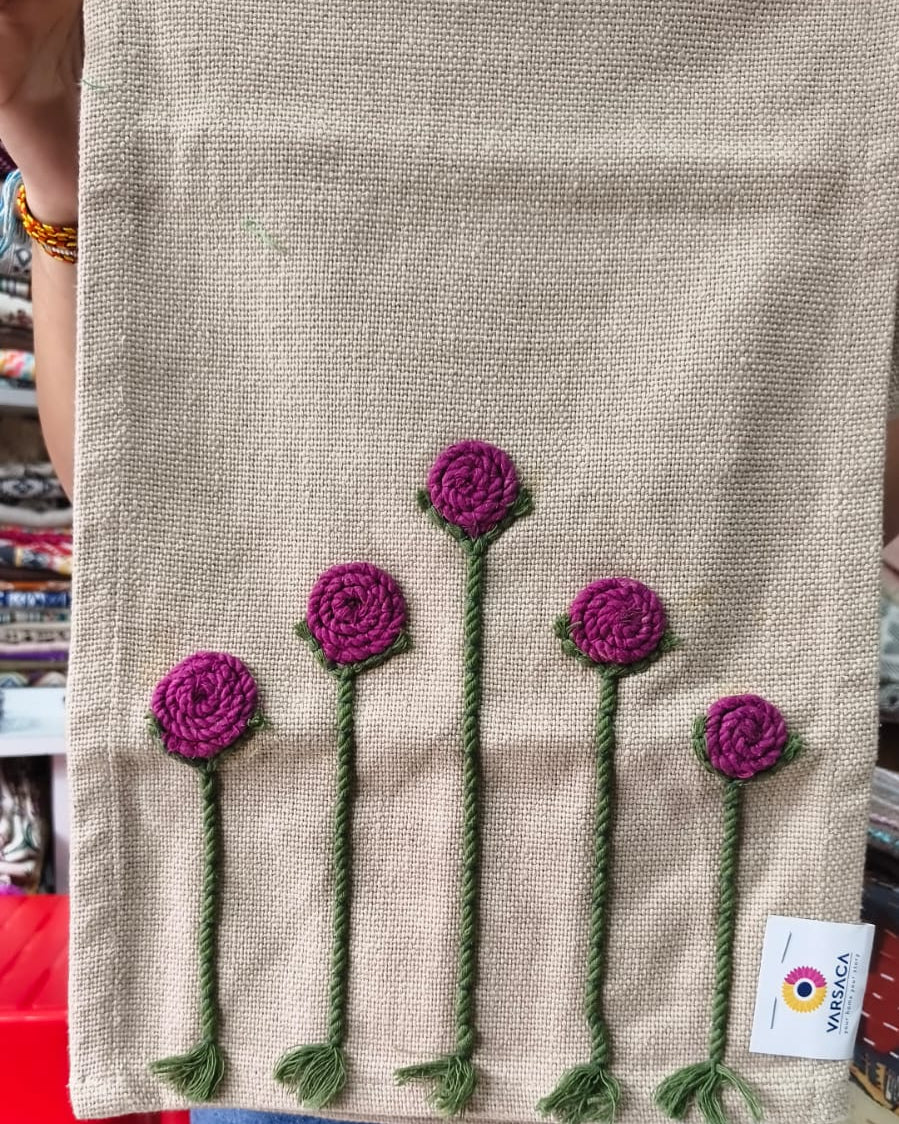Natural beige jute-cotton handloom table runner featuring handcrafted 3D magenta flower embroidery with green stems, with a Vasaca brand label.