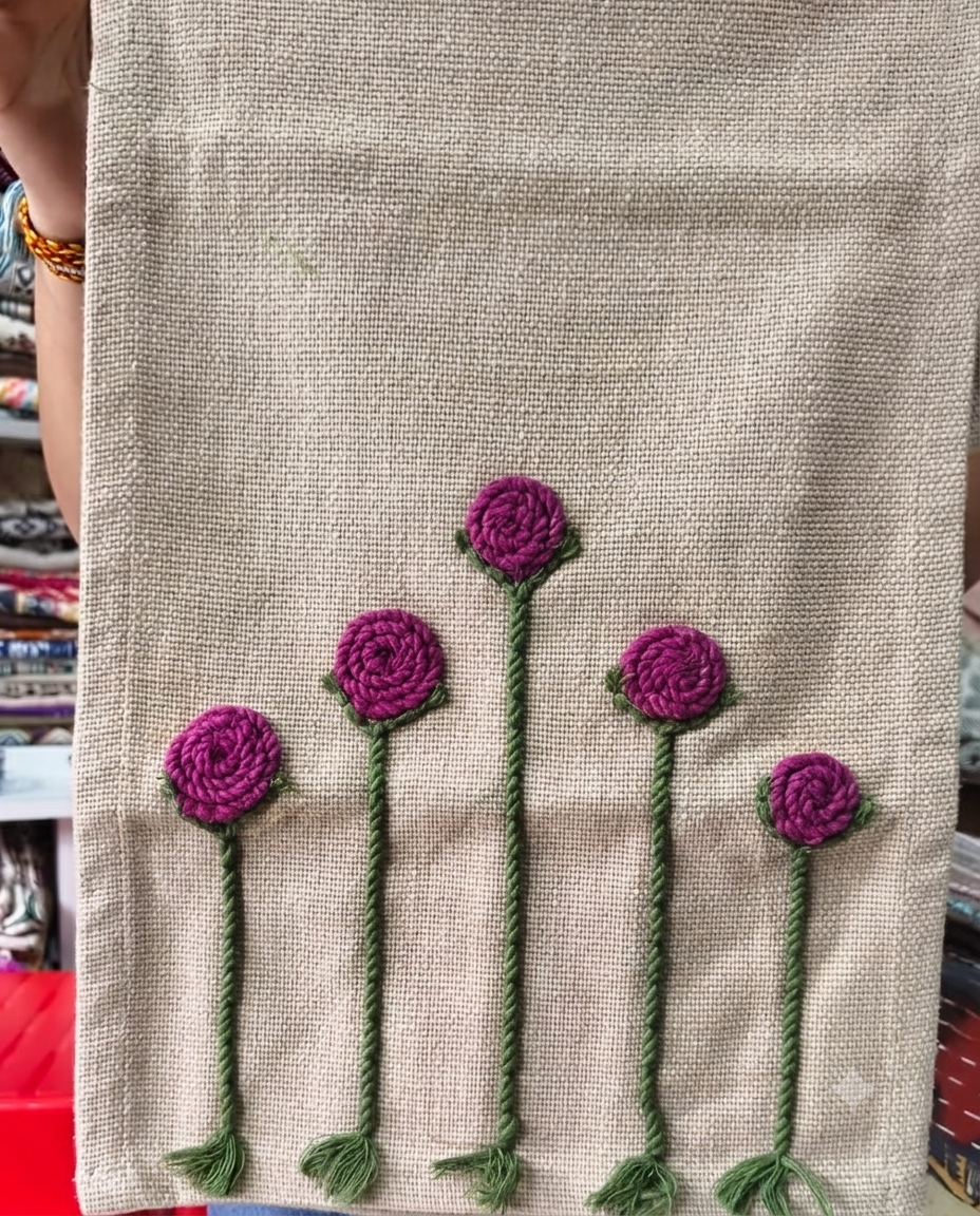 Natural beige jute-cotton handloom table runner featuring handcrafted 3D magenta flower embroidery with green stems, with a Vasaca brand label.