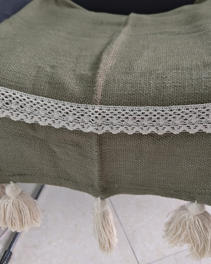 Olive green handwoven cotton wool sofa throw cover featuring a cream crochet lace trim band and thick off-white yarn tassels on a chair.