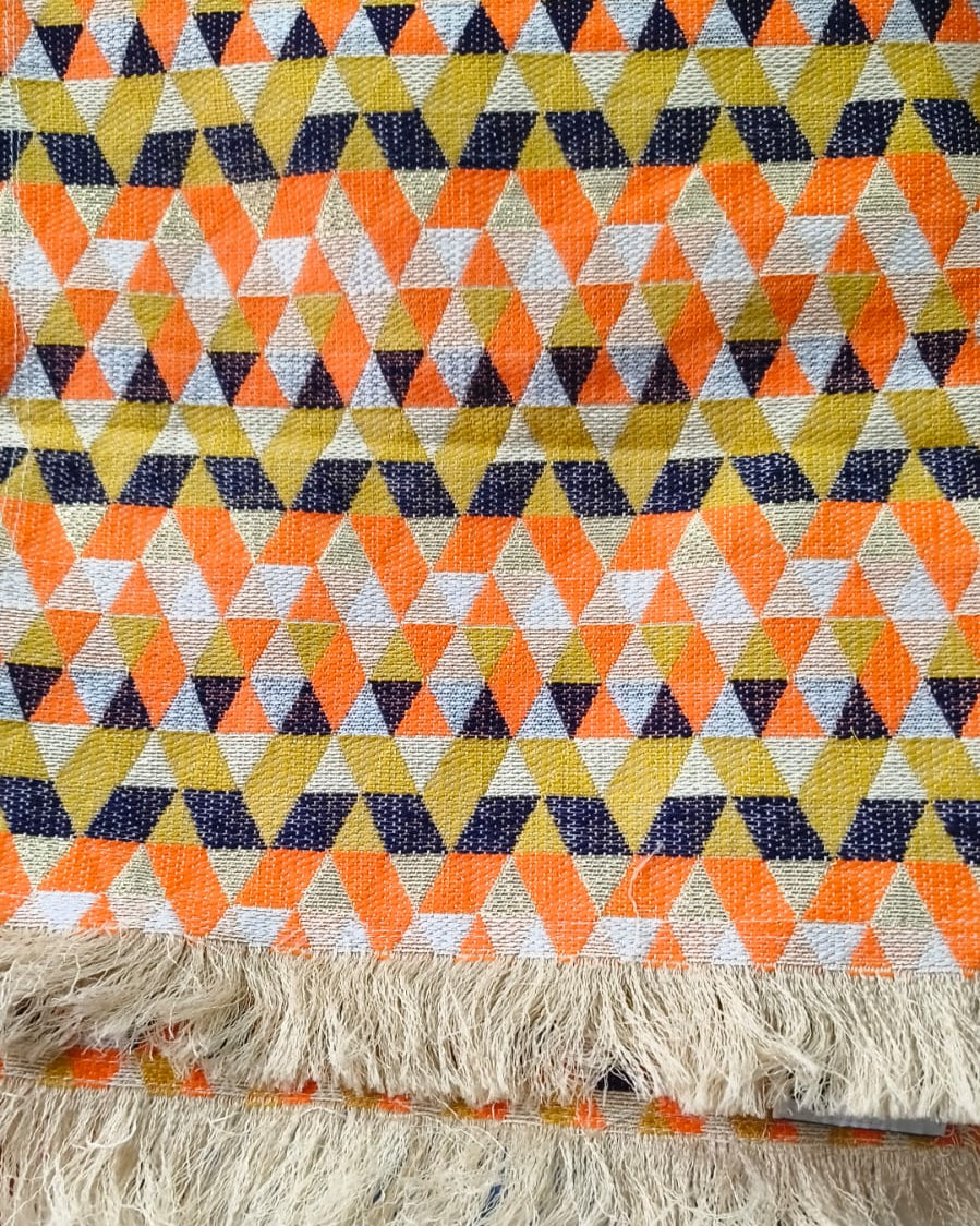 Orange geometric Jacquard cotton dining table runner featuring a vibrant triangle mosaic pattern and a textured fringe hem, with Vasaca brand labels.