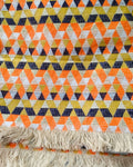 Orange geometric Jacquard cotton dining table runner featuring a vibrant triangle mosaic pattern and a textured fringe hem, with Vasaca brand labels.