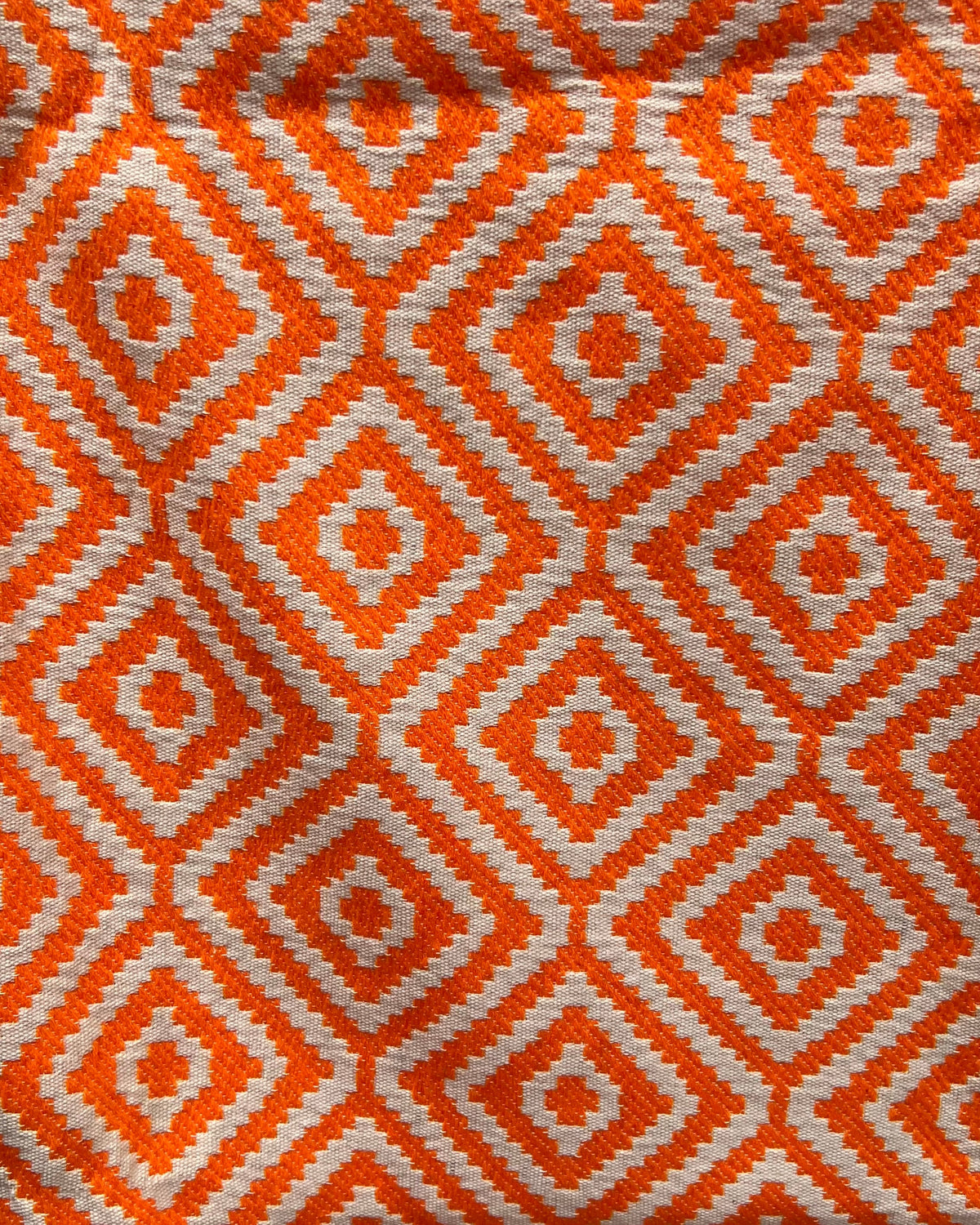 Orange and white geometric diamond pattern handloom cotton table cover featuring decorative fringe tassels along the edge.