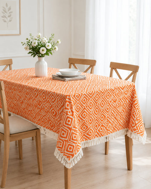 Orange and white geometric diamond pattern handloom cotton table cover featuring decorative fringe tassels along the edge.