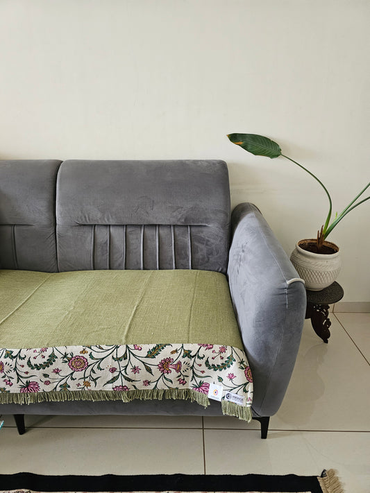 Gray cushioned sofa with a plant and decorative sofa cover against a tiled wall.