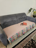 Gray and pink sofa with a colorful patterned throw blanket on a white surface.