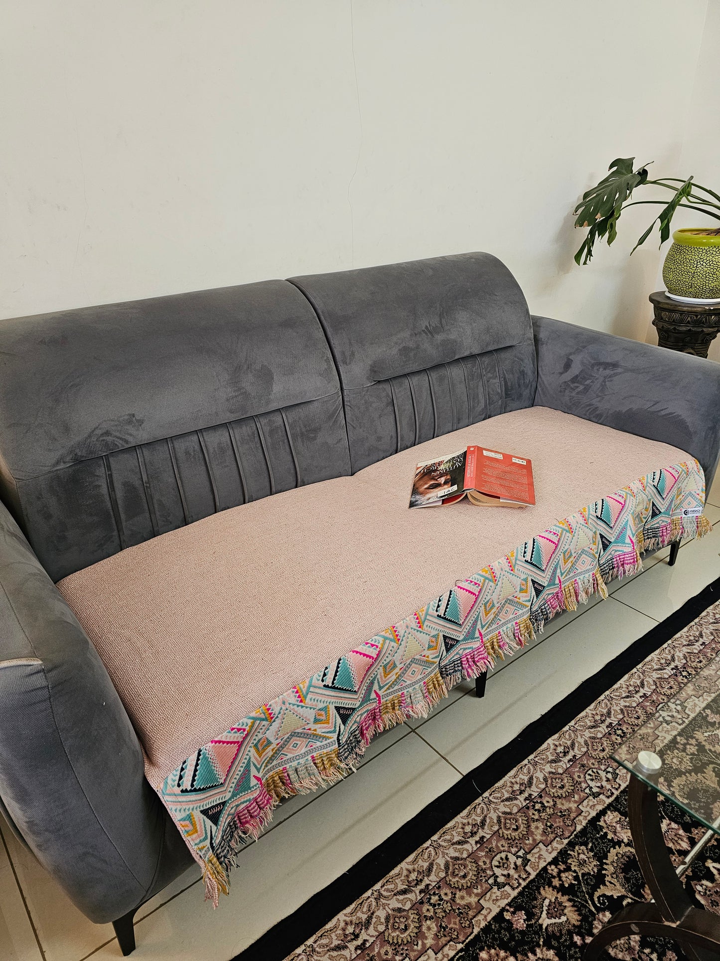 Gray and pink sofa with a colorful patterned throw blanket on a white surface.