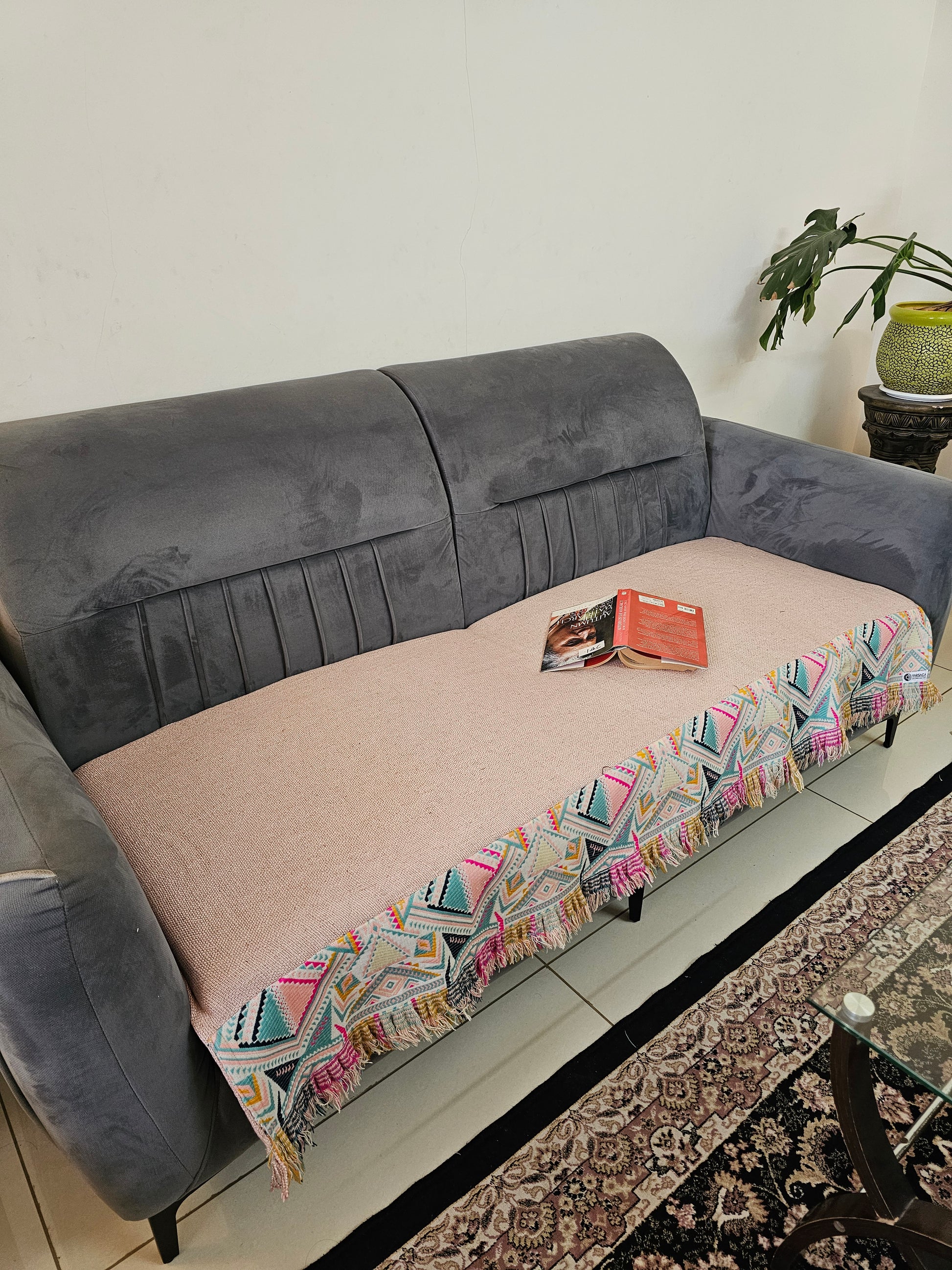 Gray and pink sofa with a colorful patterned throw blanket on a white surface.