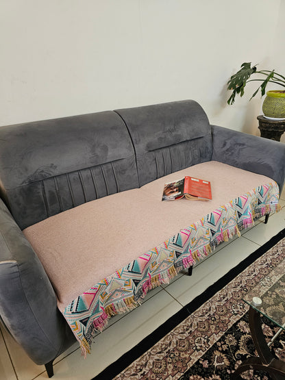 Gray and pink sofa with a colorful patterned throw blanket on a white surface.