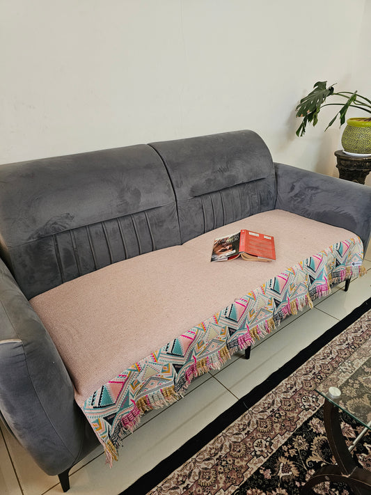 Gray and pink sofa with a colorful patterned throw blanket on a white surface.