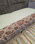 Light sage mint green jute cotton sofa seating cover featuring a vintage floral tapestry patchwork border with fringed tassels on a grey velvet sofa.