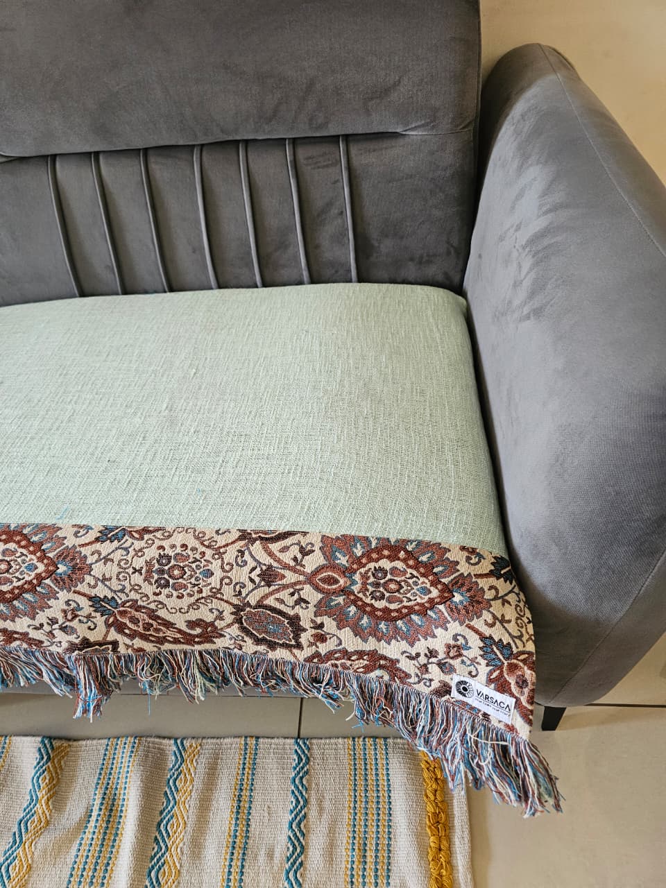 Light sage mint green jute cotton sofa seating cover featuring a vintage floral tapestry patchwork border with fringed tassels on a grey velvet sofa.