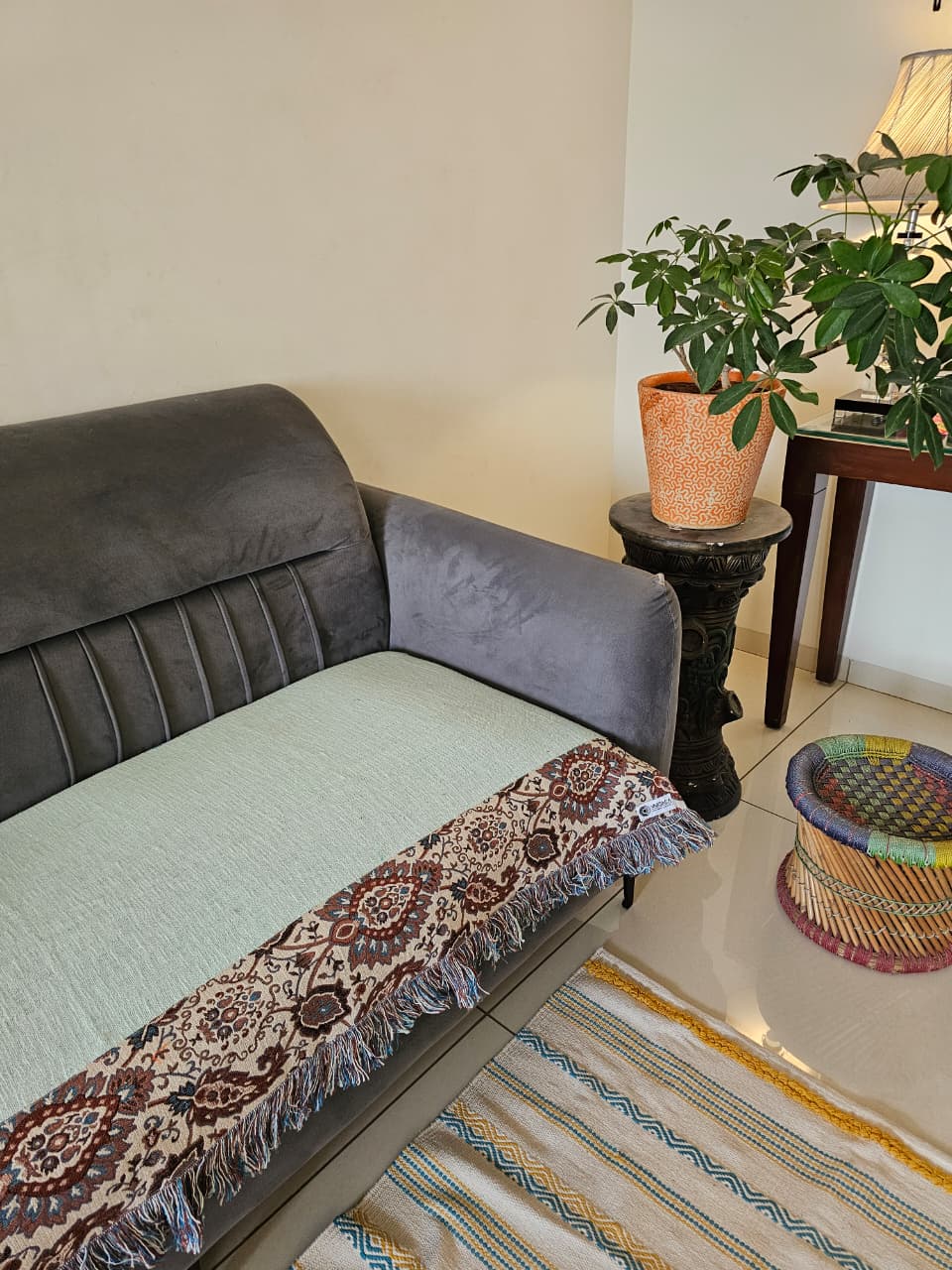 Light sage mint green jute cotton sofa seating cover featuring a vintage floral tapestry patchwork border with fringed tassels on a grey velvet sofa.