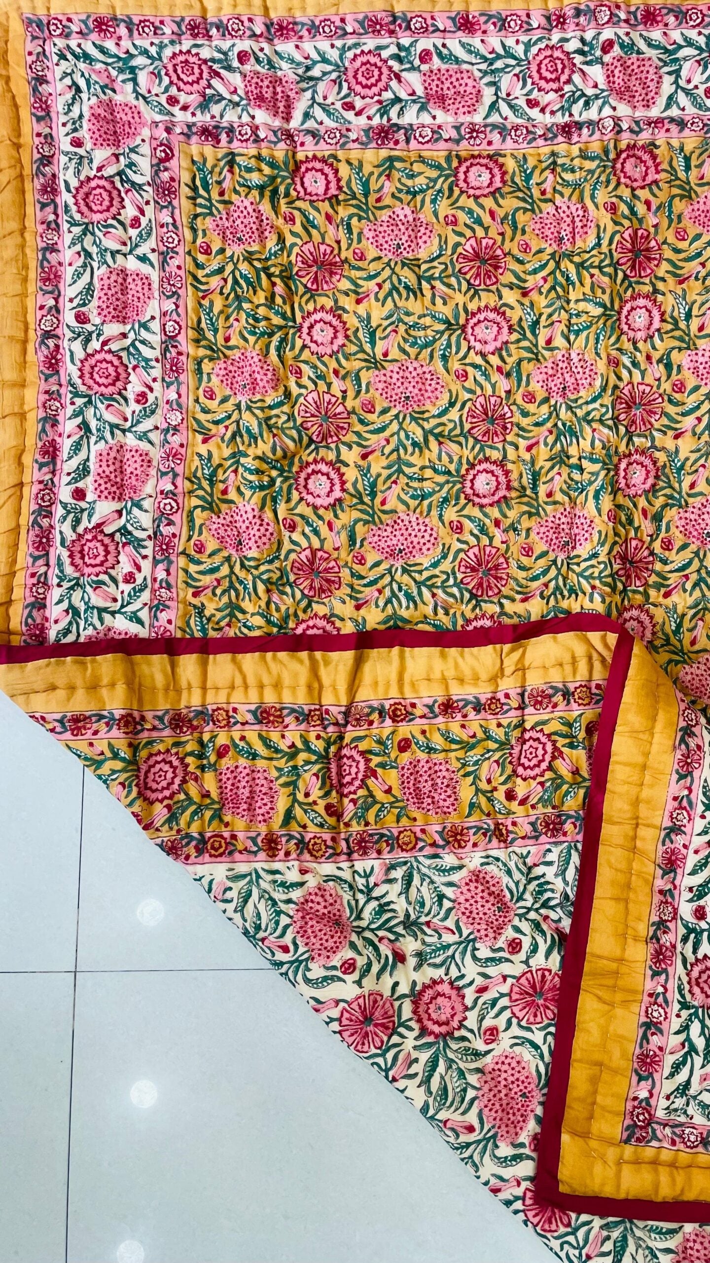 Colorful floral-patterned fabric with yellow border on a white floor.