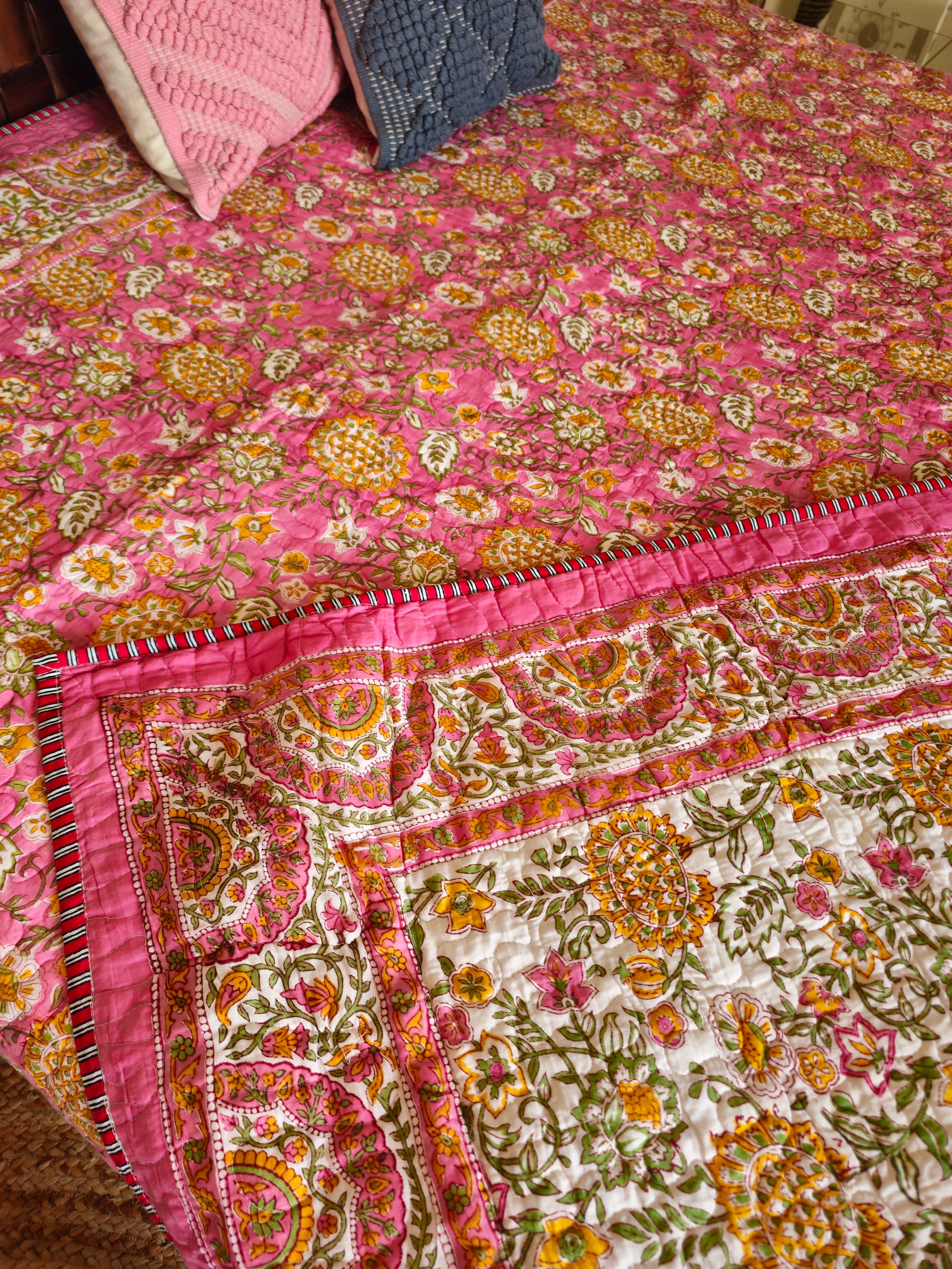 Colorful floral-patterned quilt on a bed with pink and blue pillows.