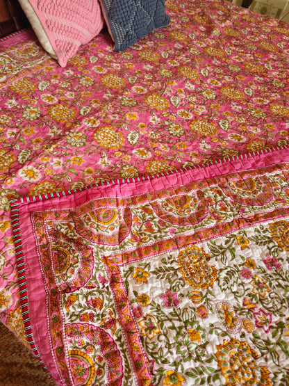 Colorful floral-patterned quilt on a bed with pink and blue pillows.
