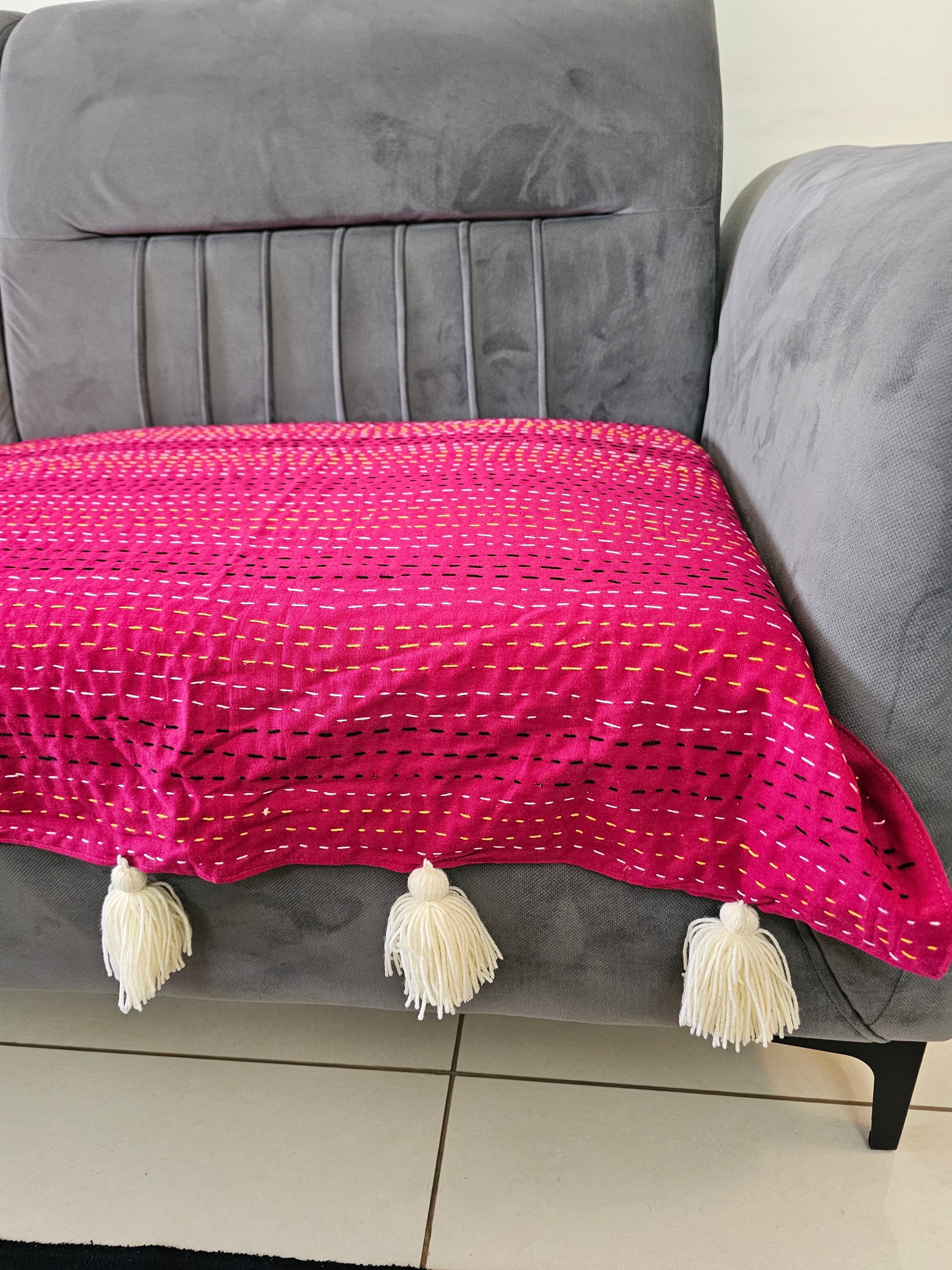 Pink textured blanket with tassels draped over a gray chair.