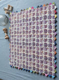 Square off-white cotton baby quilt featuring dense purple owl prints, hand-stitched Kantha quilting, and a multi-colored sawtooth triangle border laid flat on a blue surface.