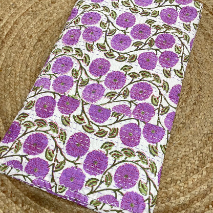 Floral patterned fabric with purple flowers and green leaves on a beige surface