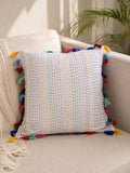 Square off-white cotton cushion cover with vertical multicolored Kantha hand stitching and vibrant rainbow tassels on a beige sofa.