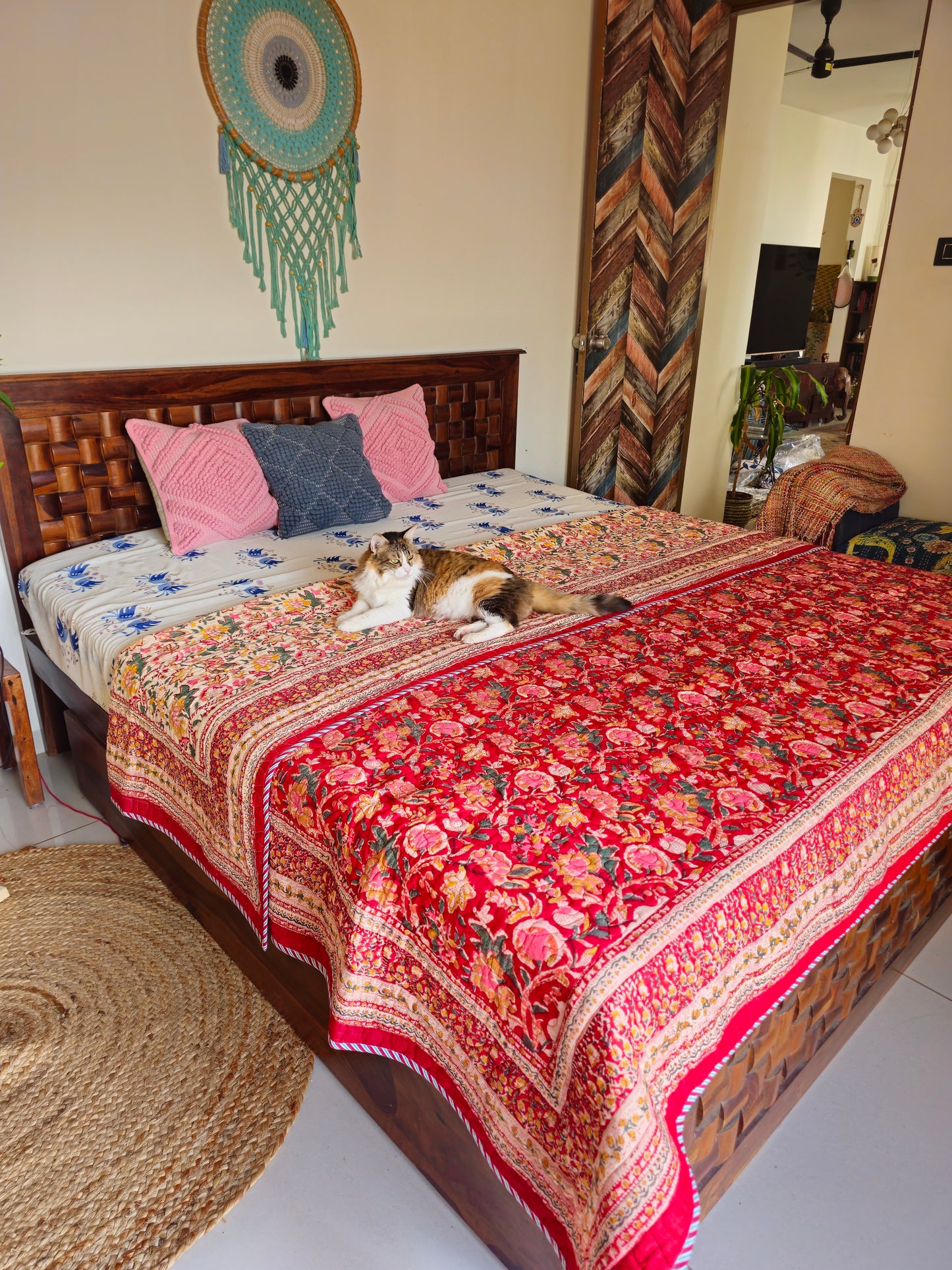 Bed with a floral quilt, pillows, and a cat in a room with decorative elements.