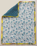 Reversible cotton baby quilt featuring a light blue beach elephant print with one corner folded over to reveal the deep teal geometric reverse side and sunny yellow binding.